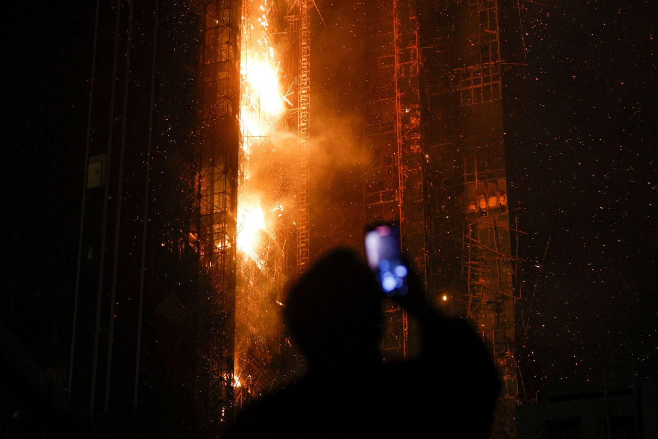 A man takes video of an under-construction skyscraper that was on fire in Hong Kong on Friday, March 3. Dozens of people were evacuated from the building, <a href=