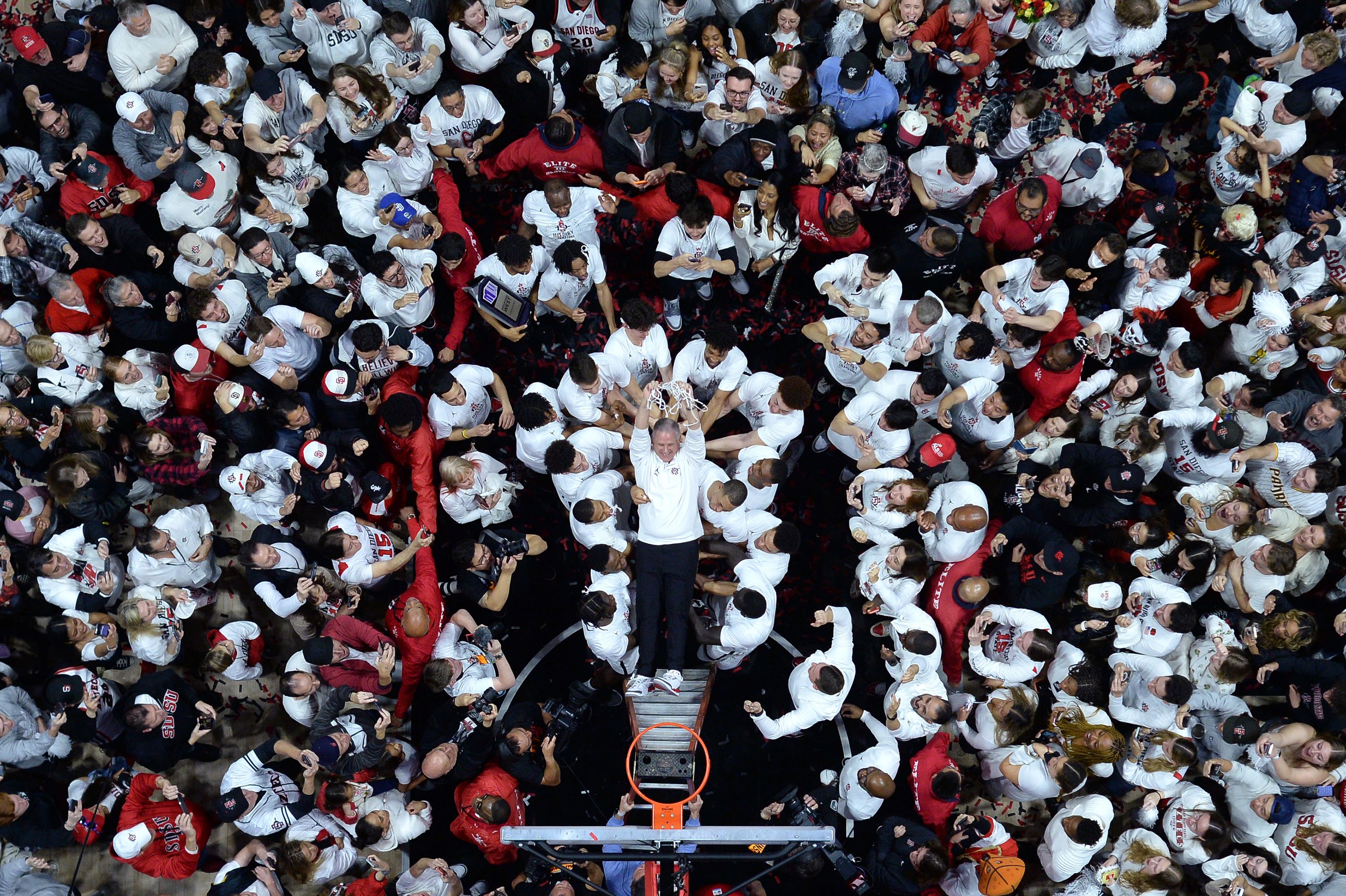 San Diego State basketball coach Brian Dutcher falls back onto his players after helping to cut down the nets at their home arena on Saturday, March 4.