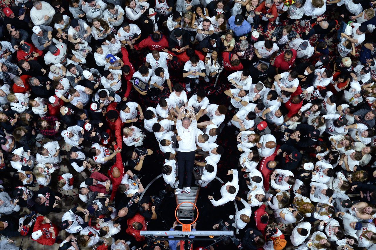 San Diego State basketball coach Brian Dutcher falls back onto his players after helping to cut down the nets at their home arena on Saturday, March 4. The Aztecs were celebrating a regular-season conference championship.