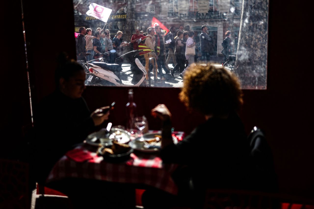 People eating lunch watch protesters march in Toulouse, France, on Thursday, March 9. Many of France's largest unions have been protesting <a href=