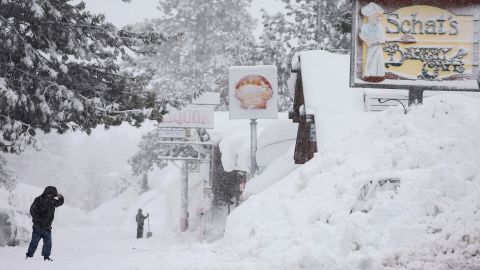 A person walks as snow falls above snowbanks piled up from previous storms during another winter storm in the Sierra Nevada mountains on March 10, 2023 in Mammoth Lakes, California.