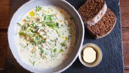 Seafood chowder, corn bread and butter in a bowl on a black board