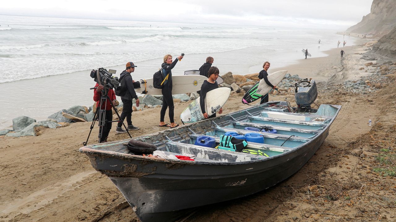 Surfers walk Sunday by a panga boat sitting along Black's Beach in San Diego.