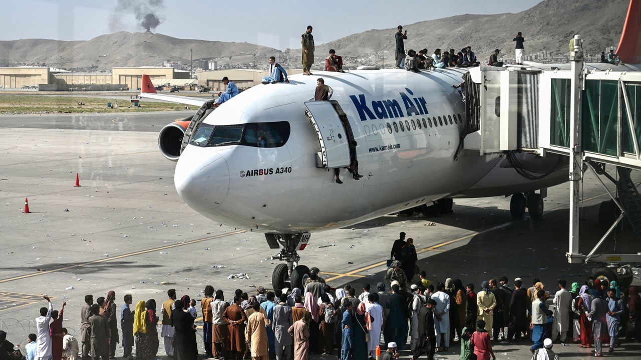 Afghans climb atop a plane as they wait at the Kabul airport on August 16, 2021, after a stunningly swift end to Afghanistan's 20-year war, as thousands of people mobbed the city's airport trying to flee the group's feared hardline brand of Islamist rule.