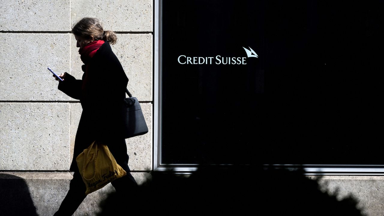 A woman is seen in silhouette walking past a branch of Switzerland's Credit Suisse bank on March 15, 2023.