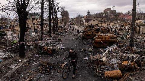 Un hombre empuja su bicicleta a través de escombros y vehículos militares rusos destrozados en una calle de Bucha, Ucrania, en abril de 2022.