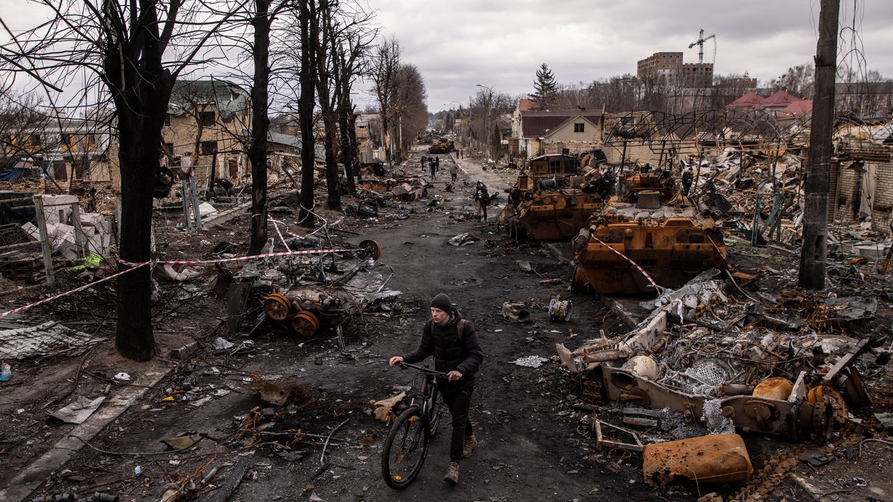 A man pushes his bike through debris and destroyed Russian military vehicles on a street in Bucha, Ukraine, in April 2022.