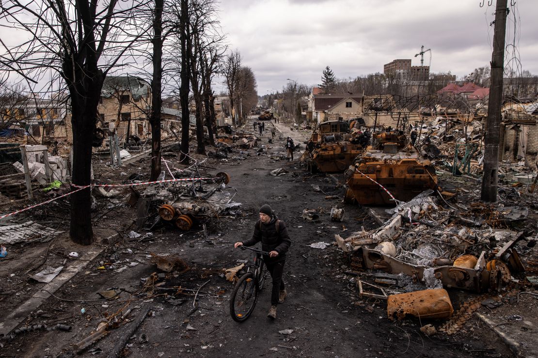 A man pushes his bike through debris and destroyed Russian military vehicles on a street in Bucha, Ukraine, in April 2022.