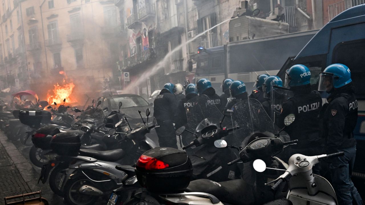 Anti-riot police move beside a truck, extinguishing the blaze of a police car.