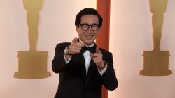 Ke Huy Quan smiles and points at the camera on the champagne carpet at the 2023 Academy Awards