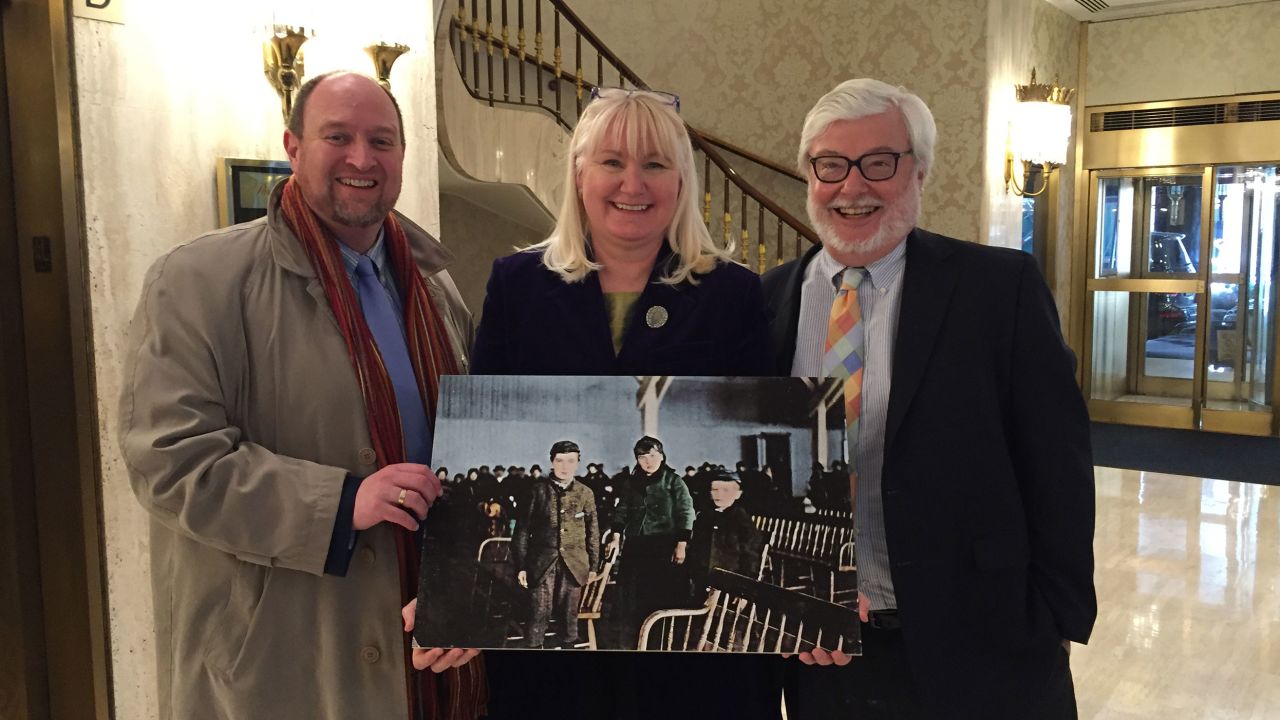 In 2016, genealogist Megan Smolenyak introduced the American and Irish branches of Annie Moore's descendants for the first time in New York. Here she stands with Paul Linehan of Kildare, Ireland, whose great grandfather was Moore's first cousin, and Michael Shulman of Chevy Chase, Maryland, whose grandfather was Moore's brother. They are holding a photo they believe shows Moore and her brothers after they arrived at Ellis Island.