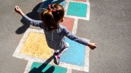 Kid girl 5 y.o. playing hopscotch on playground outdoors.