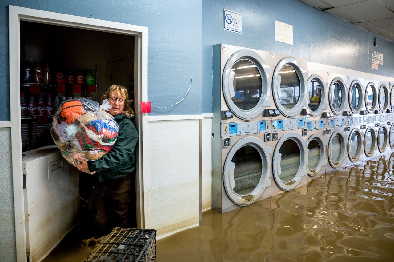 Pamela Cerruti carries a trash bag filled with clothing while wading through floodwaters at a laundromat in Monterey County, California, on Tuesday, March 14. The state faced severe flooding after <a href=