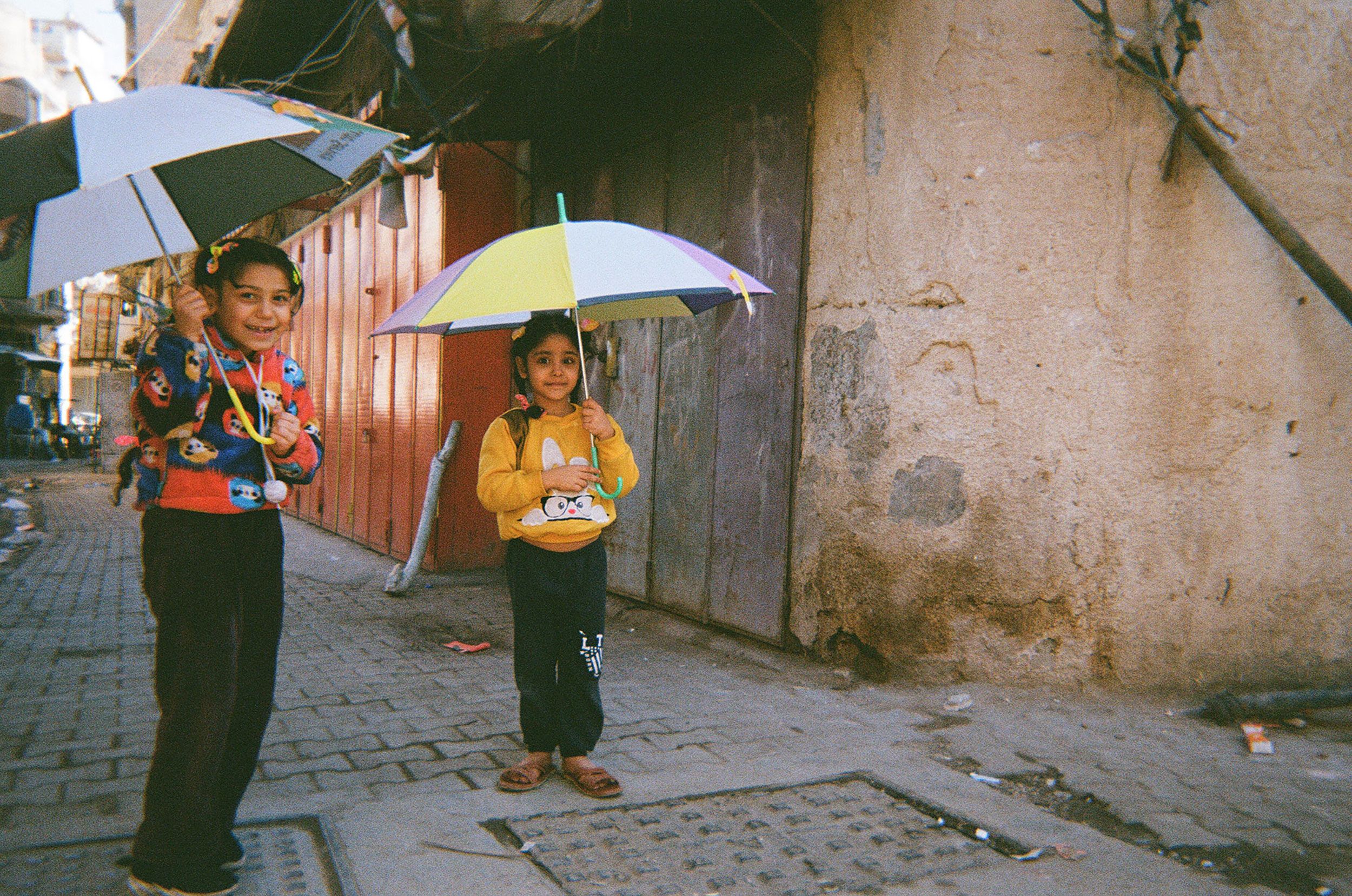 Two girls play with umbrellas on a narrow street in Baghdad.