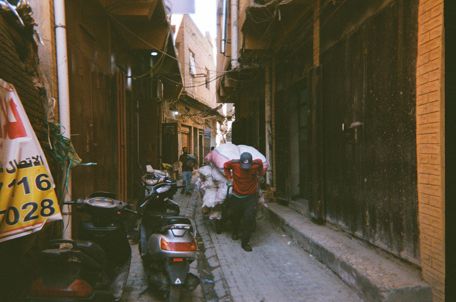 A man transports goods to a commercial market on a narrow alley in the Haydar Khana area of Baghdad. "It's my father's profession," Karim said. "He told me, 'This guy was just like me, working to carry things from merchants to customers.'"<br /><br />While Karim says he was fortunate because he comes from a well-to-do family, that doesn't mean is childhood in Iraq was rosy. He was 10 years old at the start of the US occupation, which went into his teen years.<br /><br />"Imagine that you are in the height of your adolescence, afraid to go out to live your life as a young teenager, and you are shocked that someone is trying to kill you [based] on your identity without knowing who you are," he said.