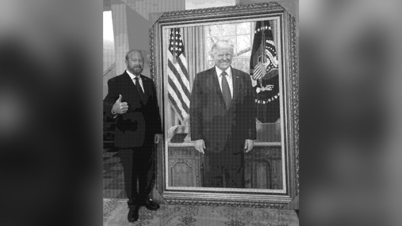 In this undated photo from an email obtained by CNN, US Ambassador to El Salvador Ronald Johnson stands with a painting of former President Donald Trump at the US Embassy in El Salvador.