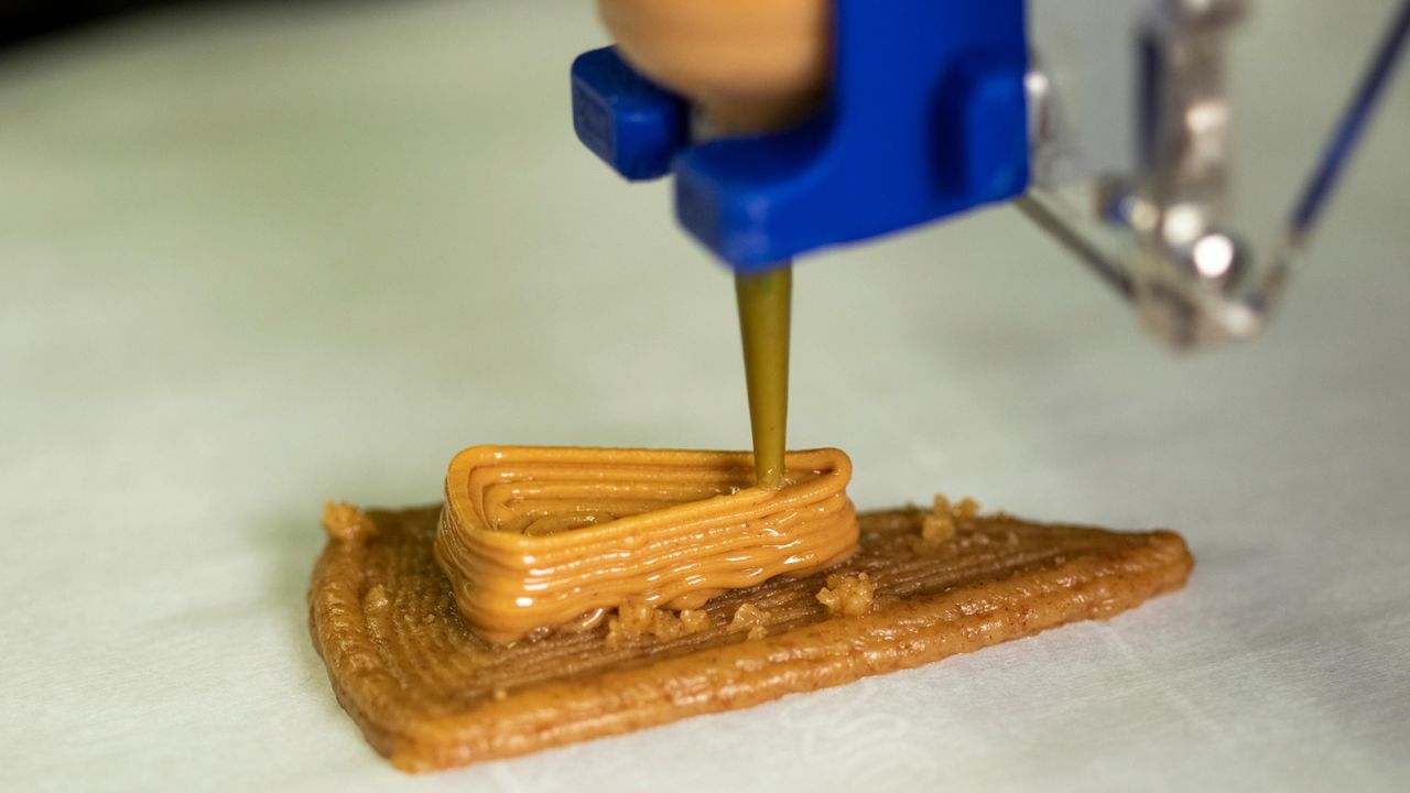 Peanut butter is deposited onto a layer of graham cracker paste as part of the 3D-printing process.