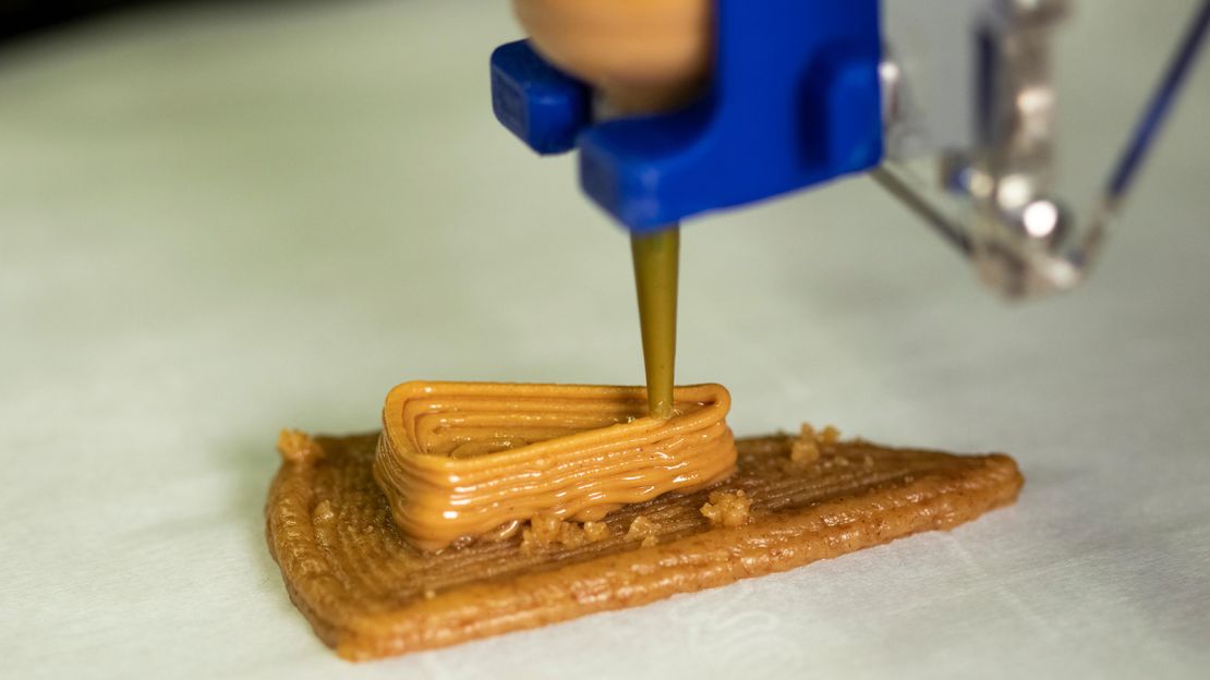Peanut butter is deposited onto a layer of graham cracker paste as part of the 3D-printing process.