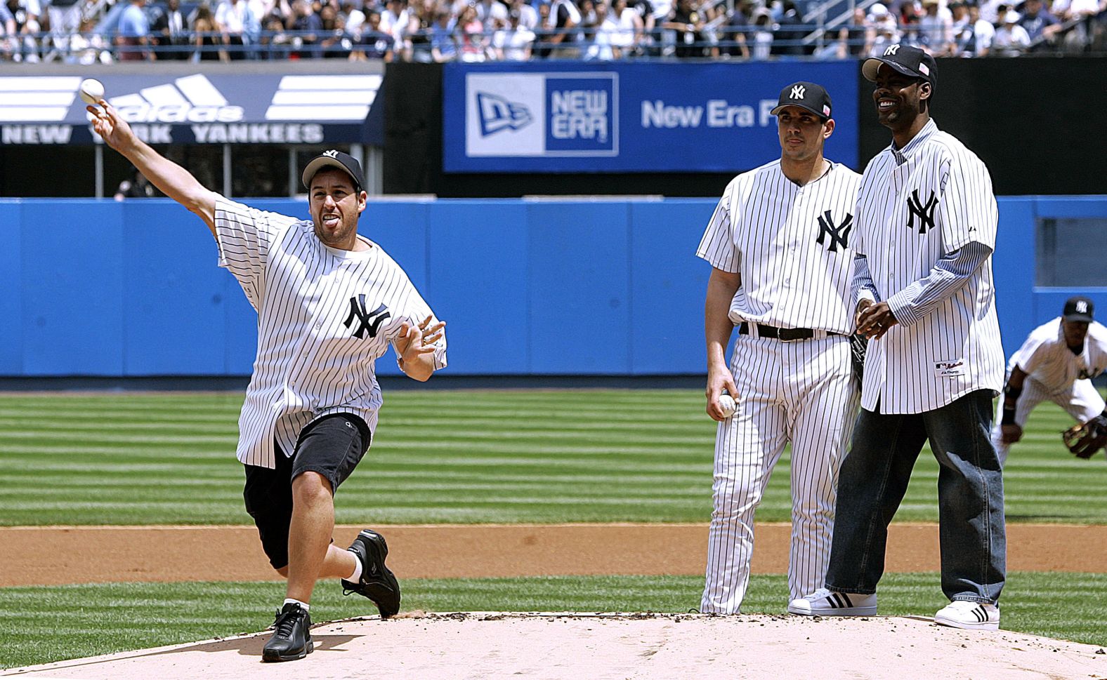 Sandler throws a pitch at Yankee Stadium before a Major League Baseball game in New York in May 2005. At right are Chris Rock and Yankees pitcher Carl Pavano.