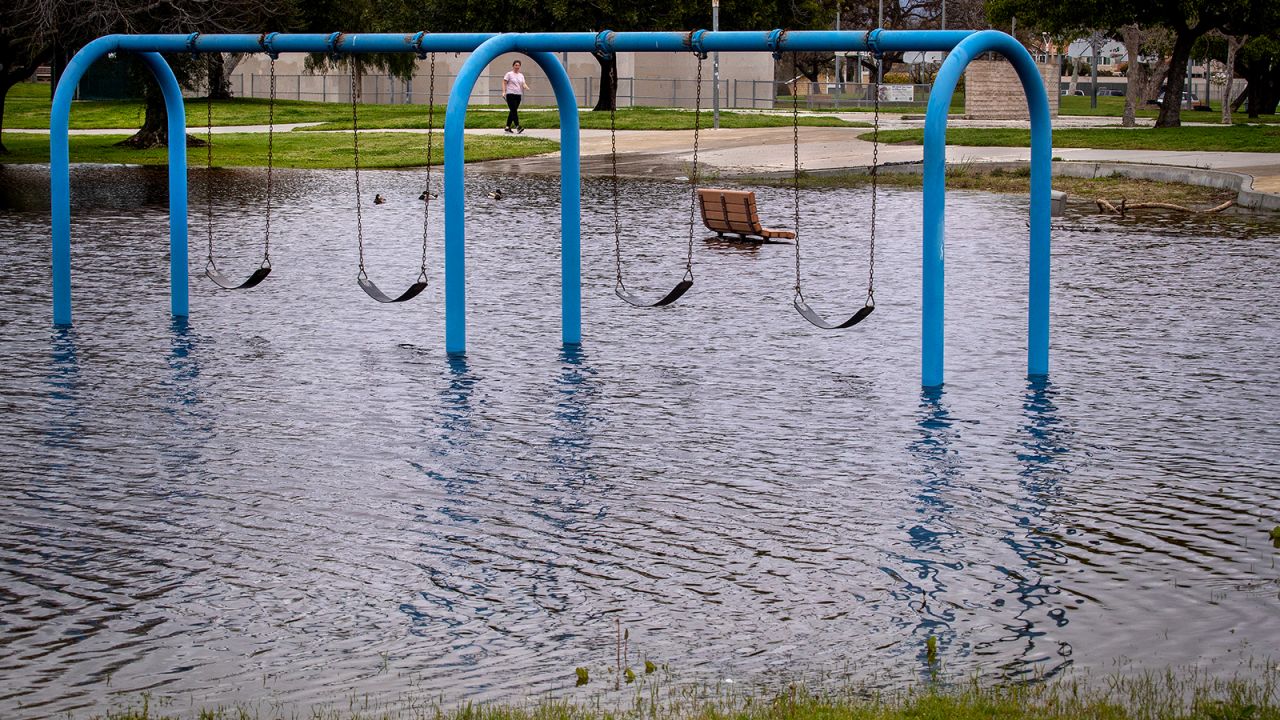 Seseorang berjalan melepasi bahagian taman permainan yang ditenggelami air di Huntington Beach pada hari Isnin, 20 Mac 2023.