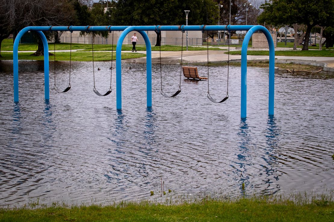 A person walks past a flooded playground section in Huntington Beach Monday, March 20, 2023.