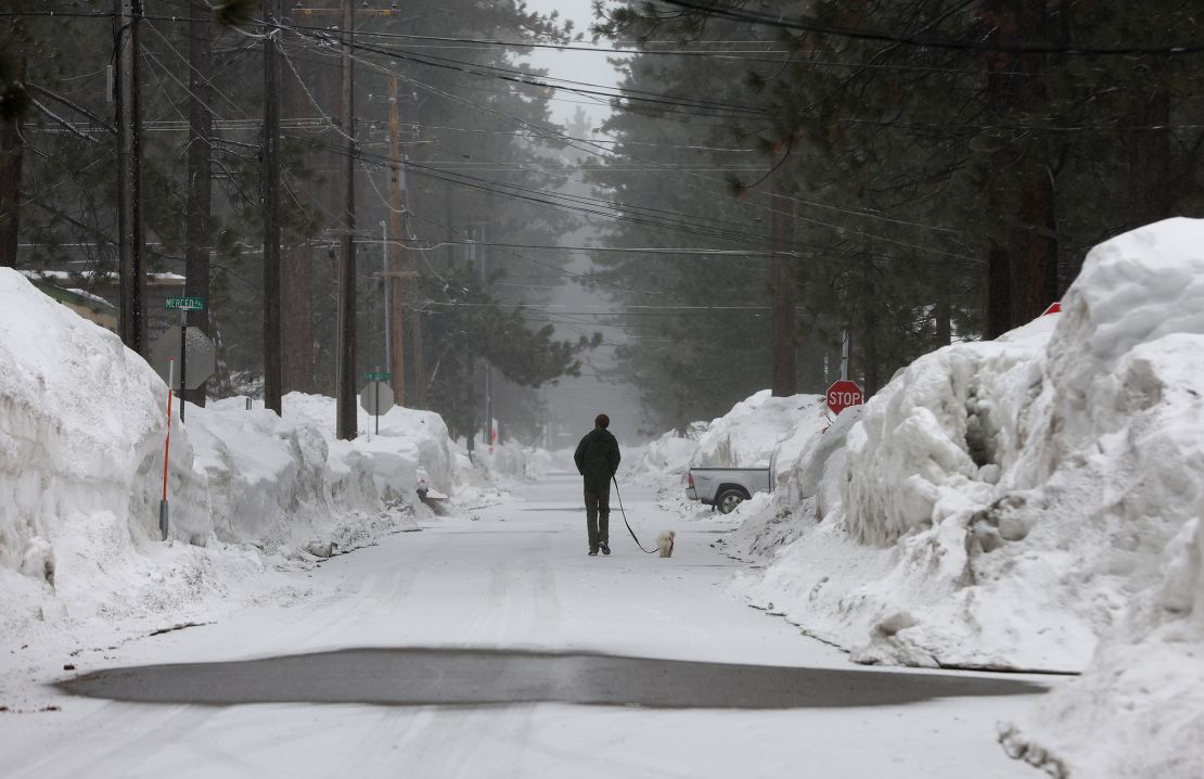 A man walks his dog on a snow covered street as snow begins to fall Tuesday in South Lake Tahoe, California. 