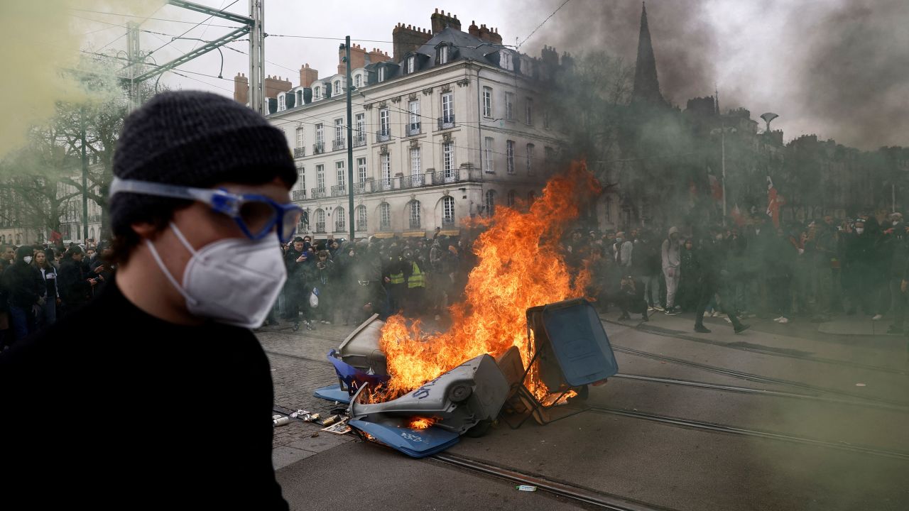 A protester stands near burning garbage bins during a demonstration as part of protests against the pension reform, in Nantes, France, March 23, 2023.