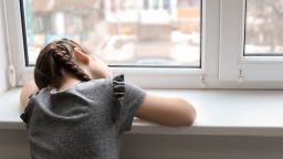Lonely little girl near window indoors. Child autism.