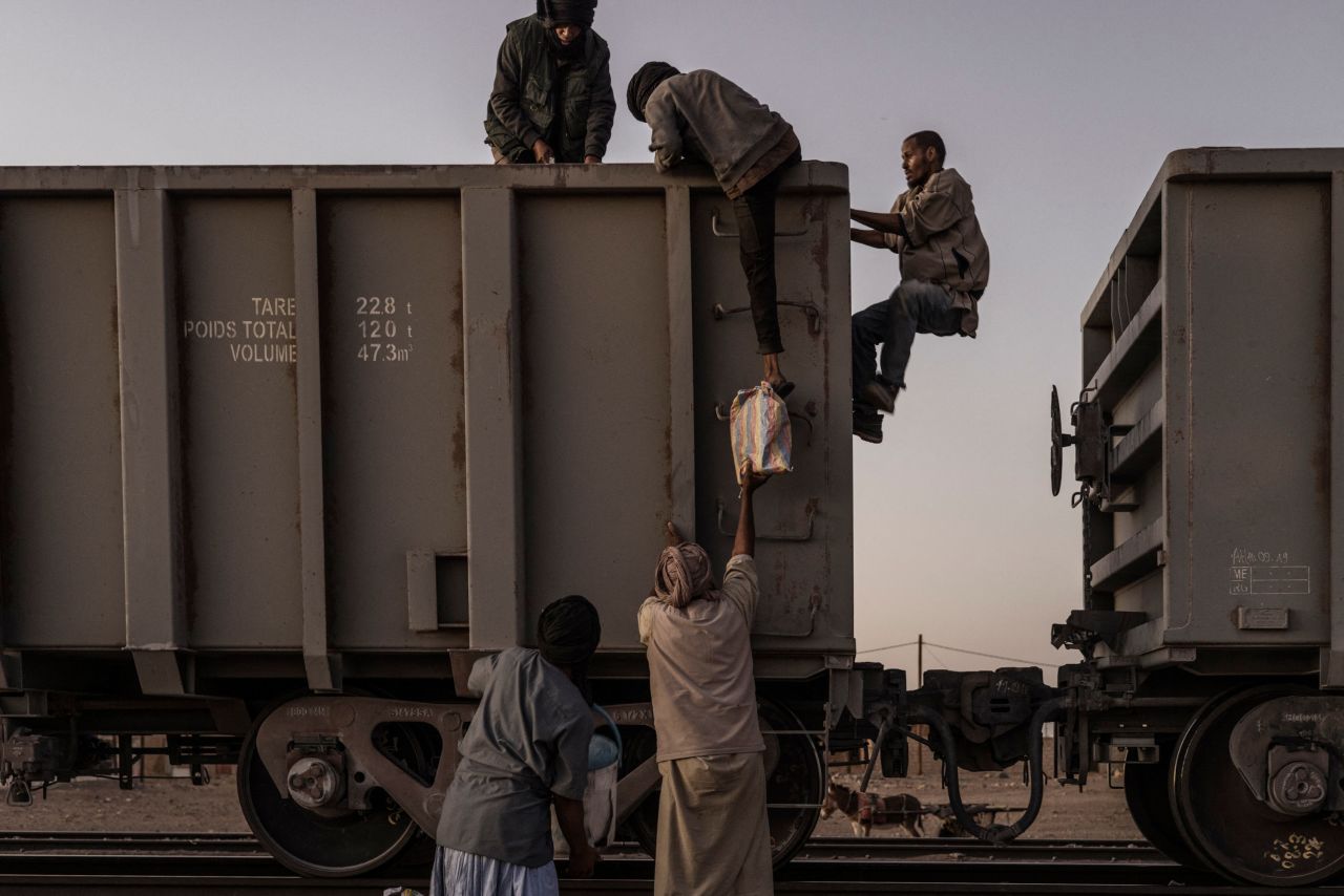 People load their belongings aboard the Iron Ore freight train as it stops at a station in Choum, Mauritania, on Sunday, March 19.