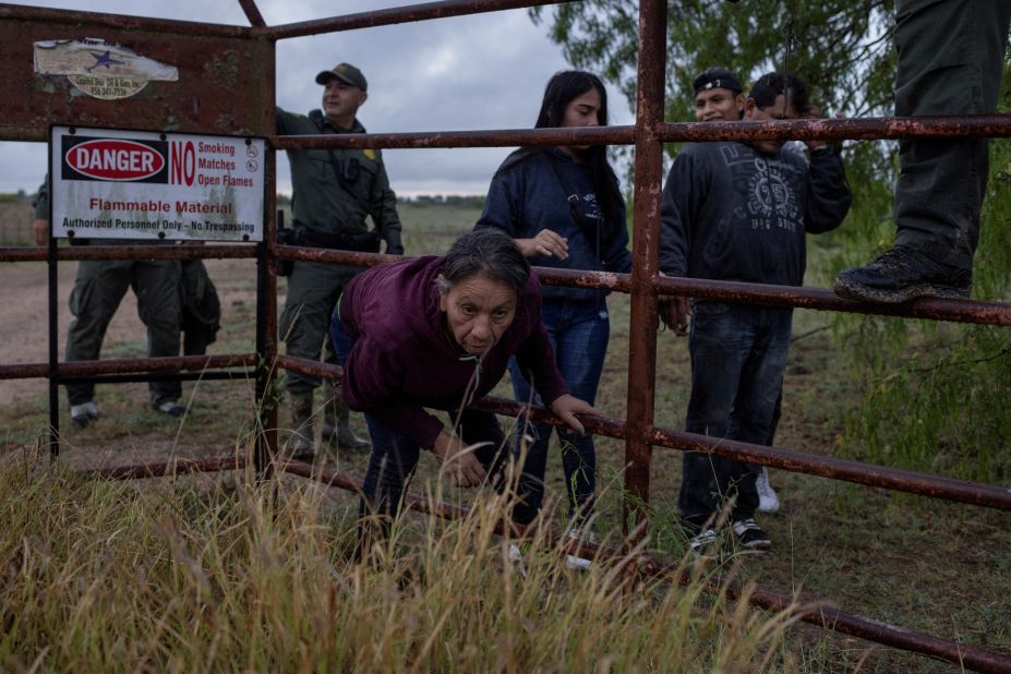 A migrant squeezes through the fence of a ranch in La Joya, Texas, where she and others were detained by US Border Patrol agents on Tuesday, March 21. They had been hiding in thick brush after crossing the Rio Grande from Mexico.