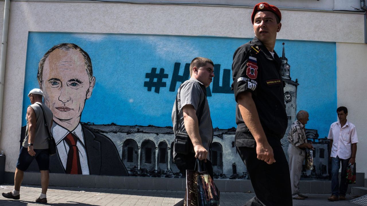 In this file photo taken in 2015, people walk by fresh graffiti depicting Vladimir Putin in Crimea.