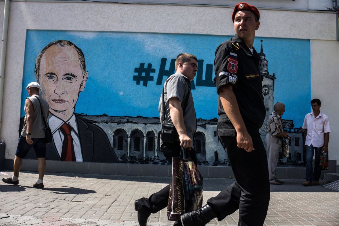 In this file photo taken in 2015, people walk by freshly painted graffiti depicting Russian President Vladimir Putin in Crimea.