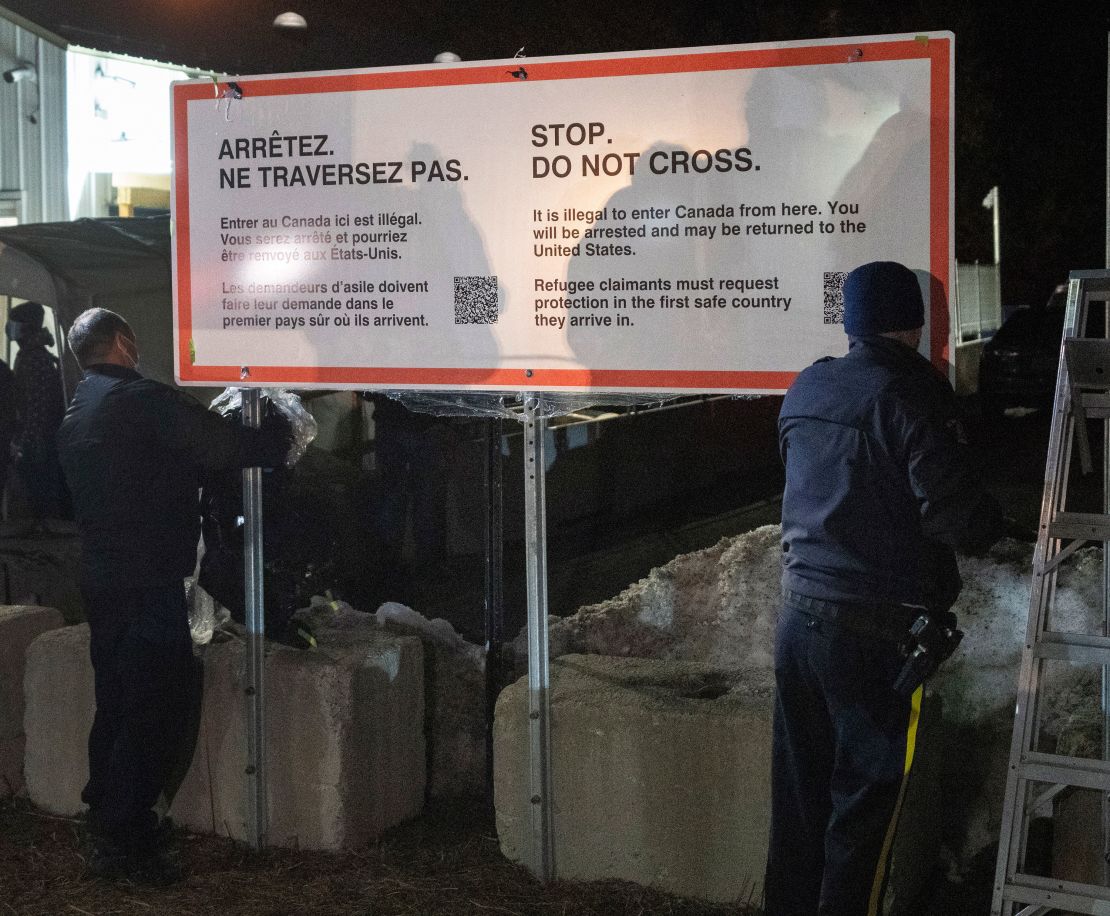 Royal Canadian Mounted Police officers unwrap a new warning sign for asylum-seekers on the border at Roxham Road from New York into Canada, early Saturday March 25, 2023, in Champlain, N.Y. 