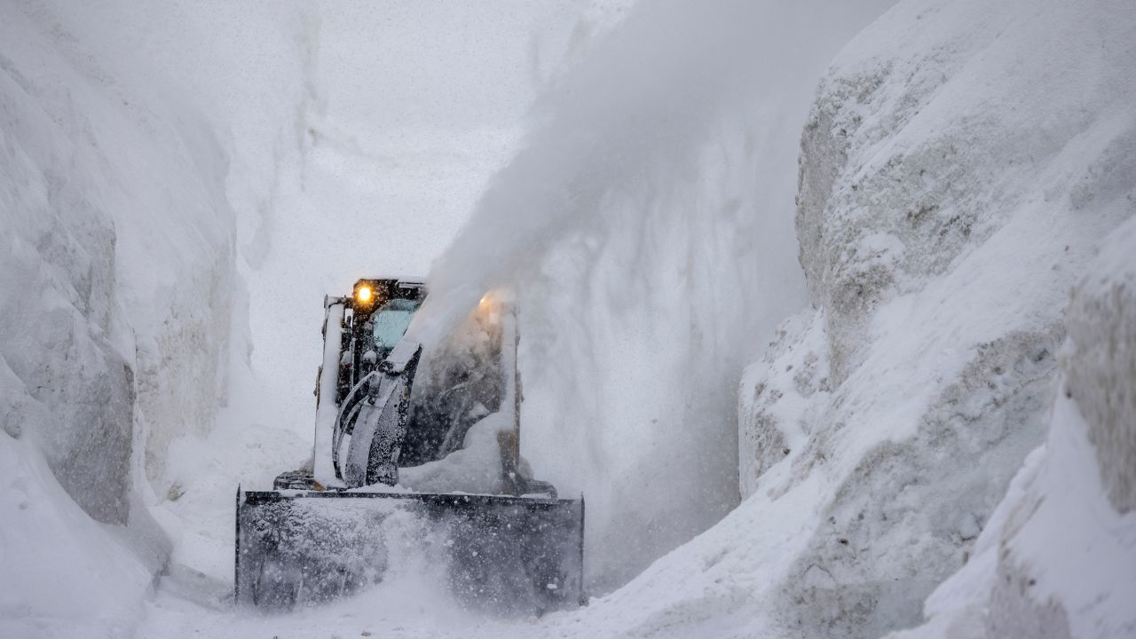 A tractor blows snow from a street that is walled in by snow as it continues to deepen in the first days of spring on March 21, in Mammoth Lakes, California.