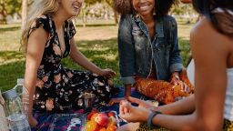 Smiling multiracial female friends having fun at picnic in the park - group of healthy friends having a picnic