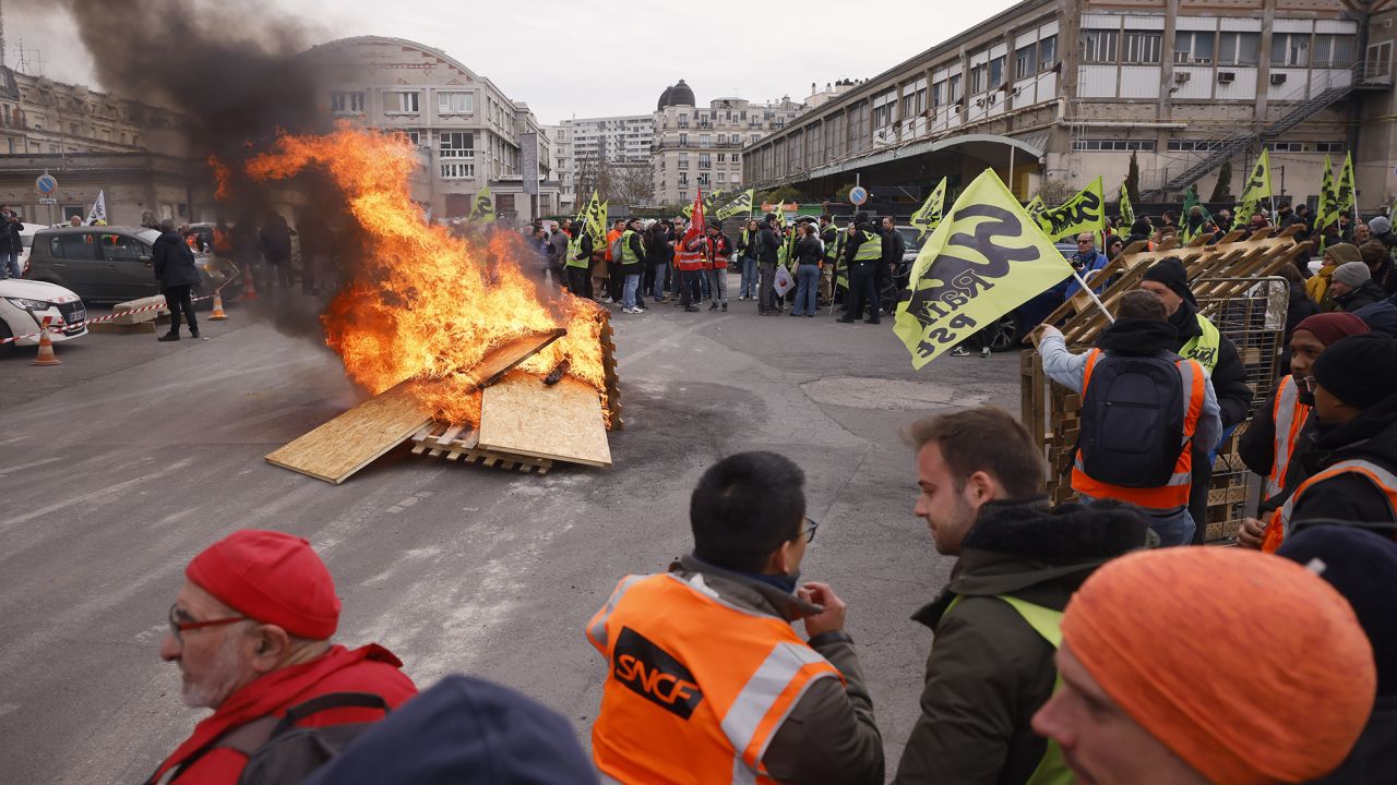 Trabajadores ferroviarios en huelga se manifiestan cerca de tablas en llamas en la estación de tren Gare de Lyon.