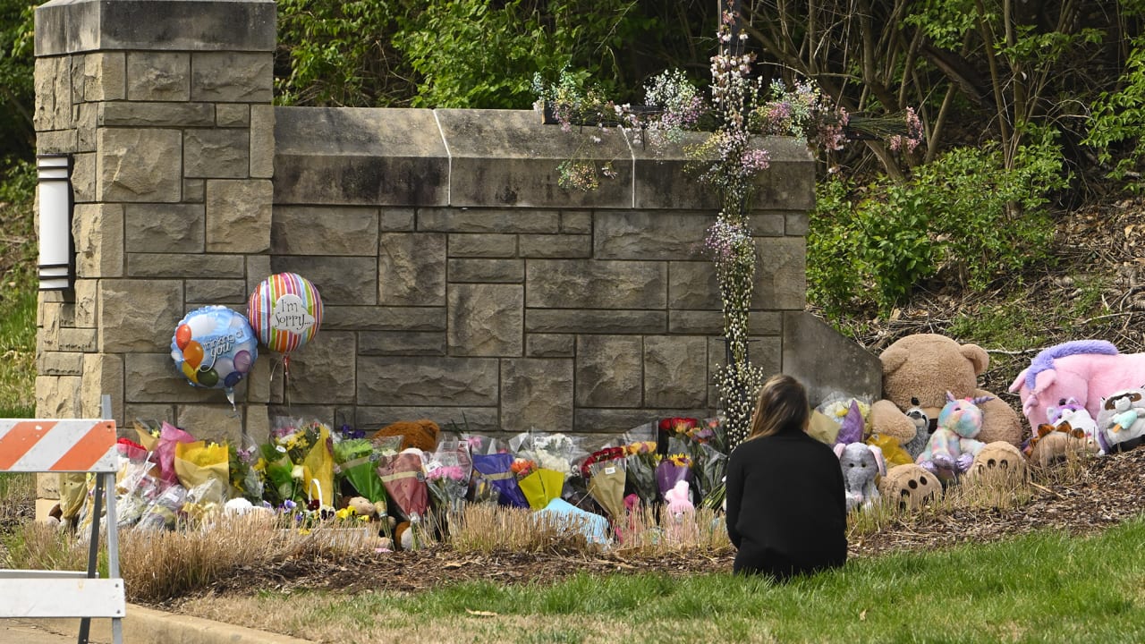 A person kneels in front of an entry to Covenant School which has become a memorial for shooting victims, Tuesday, March 28, 2023, in Nashville, Tenn.