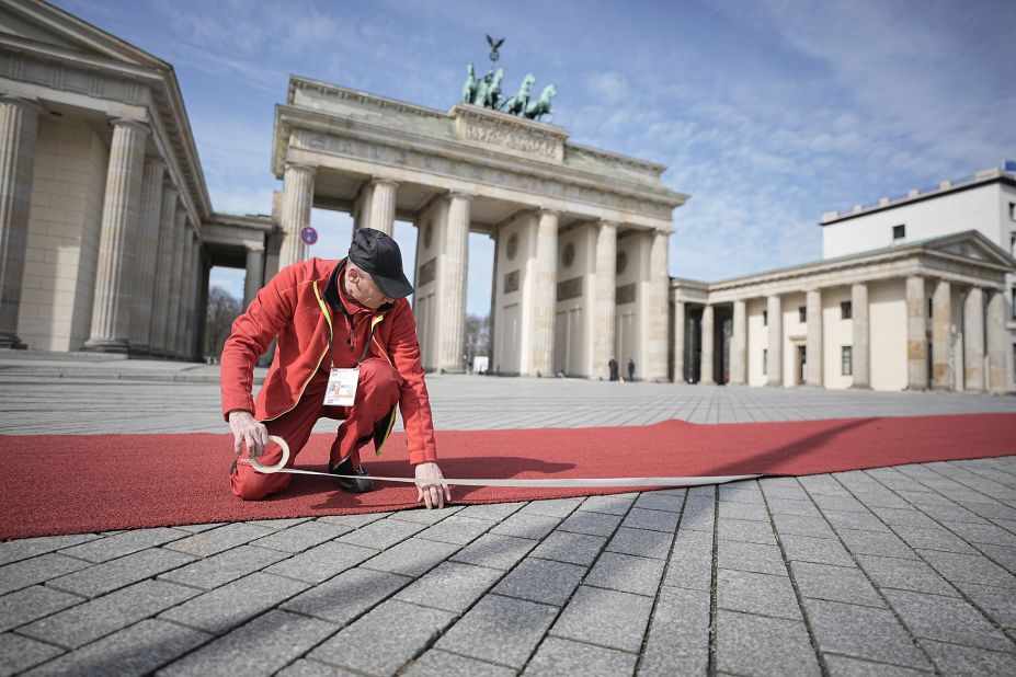 A man fastens a red carpet in front of the Brandenburg Gate.