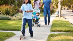 Couple Push Daughter In Stroller As Son Rides Scooter