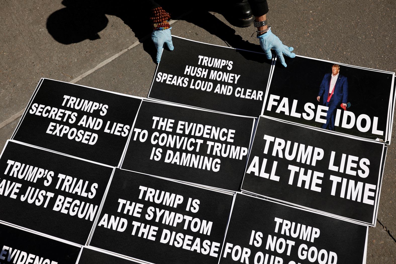 A person places signs on the ground as anti-Trump protesters gathered outside the Manhattan Criminal Courthouse on March 27, 2023.
