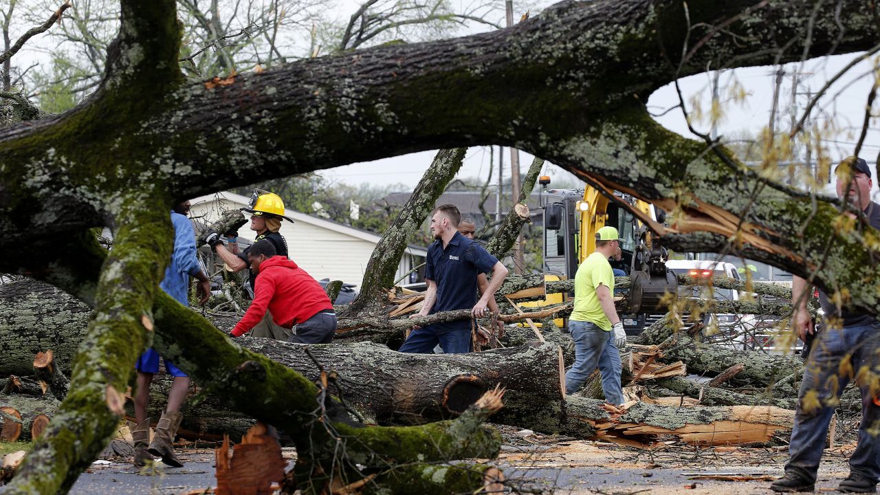 Police and firefighters get help from volunteers clearing downed trees on Keihl Avenue after storms ripped through the area on Friday, March 31, in Sherwood, Arkansas.