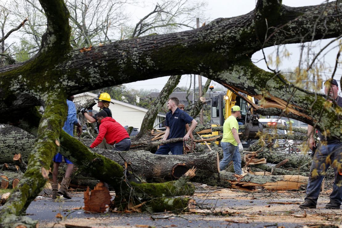 Police and firefighters get help from volunteers clearing downed trees on Keihl Avenue after storms ripped through the area on Friday, March 31, in Sherwood, Arkansas.