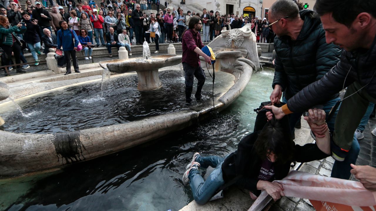 An environmental activist is removed from the ''Fontana della Barcaccia'' by police as the other activist pours black paint inside the fountain in Rome on Saturday, April 1, 2023. 