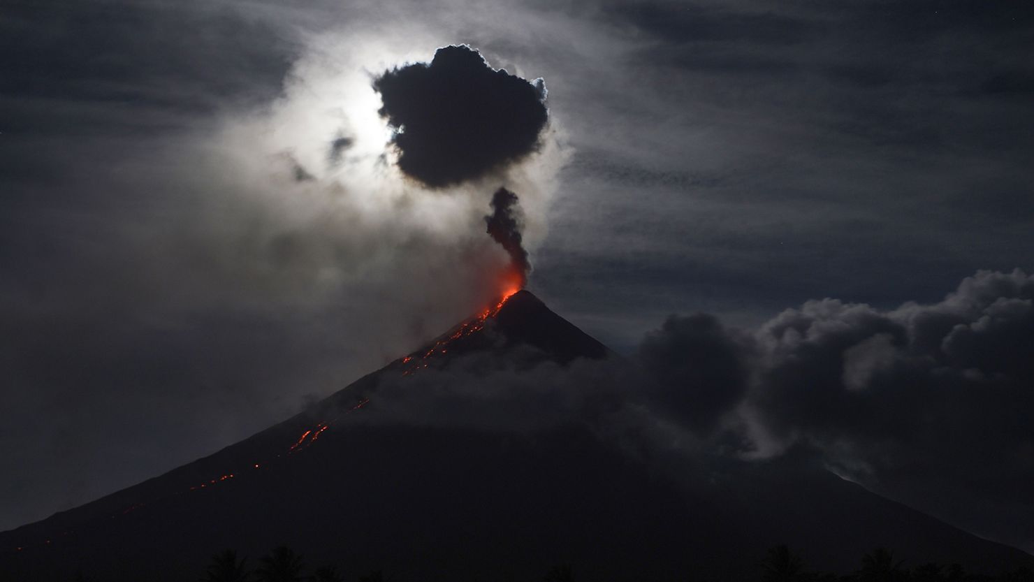 The moon, obscured by clouds, illuminates the Mayon volcano as it spews ash near Legazpi City in the Philippines on February 1, 2018.