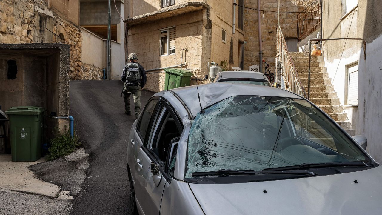 An Israeli police bomb disposal unit member walks past a damaged car, after rocket fire was launched from Lebanon and intercepted by Israel on Thursday.