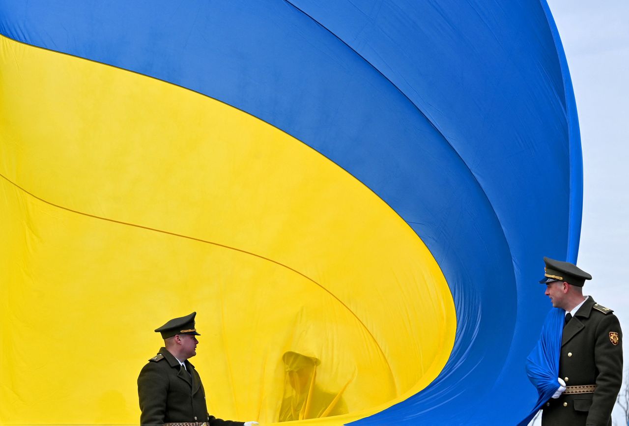 Ukrainian servicemen hold a huge national flag during a ceremony in Bucha, Ukraine, on Friday, March 31. Friday marked the <a href=