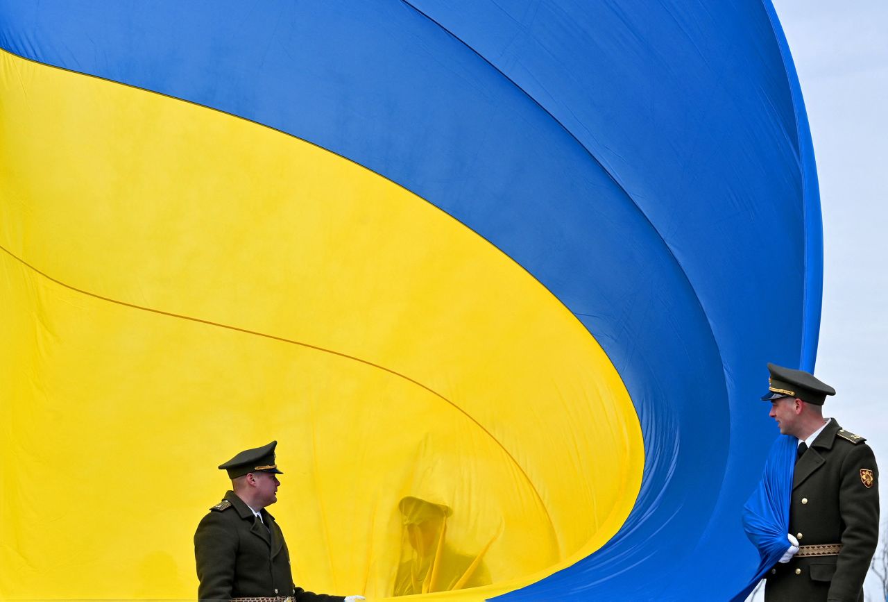 Ukrainian servicemen hold a huge national flag during a ceremony in Bucha, Ukraine, on Friday, March 31. Friday marked the one-year anniversary of the liberation of Bucha, a town that has become synonymous with Russia's brutal occupation and alleged war crimes.