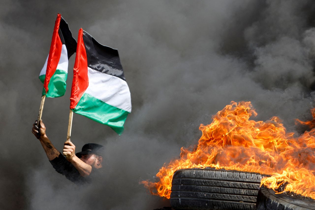A demonstrator holds Palestinian flags next to burning tires during a protest at the Israel-Gaza border fence on Wednesday, April 5.