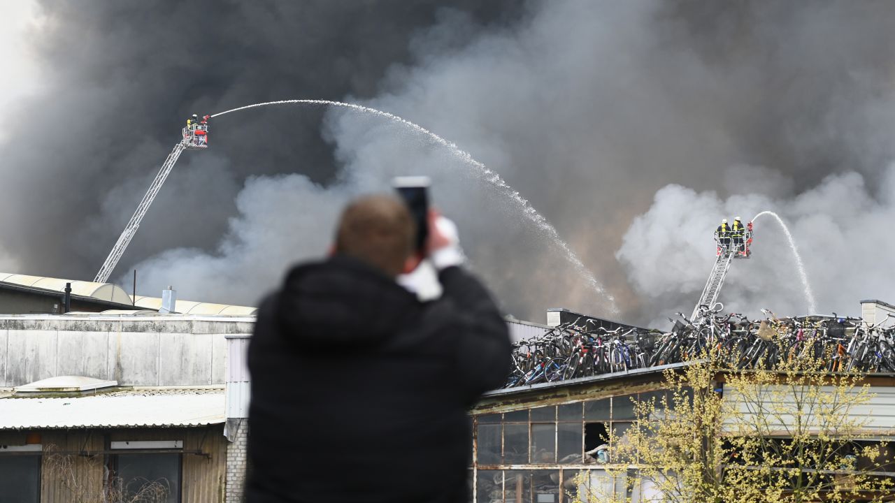A man photographs firefighters spraying water from aerial ladders onto the burning warehouse on Sunday. 
