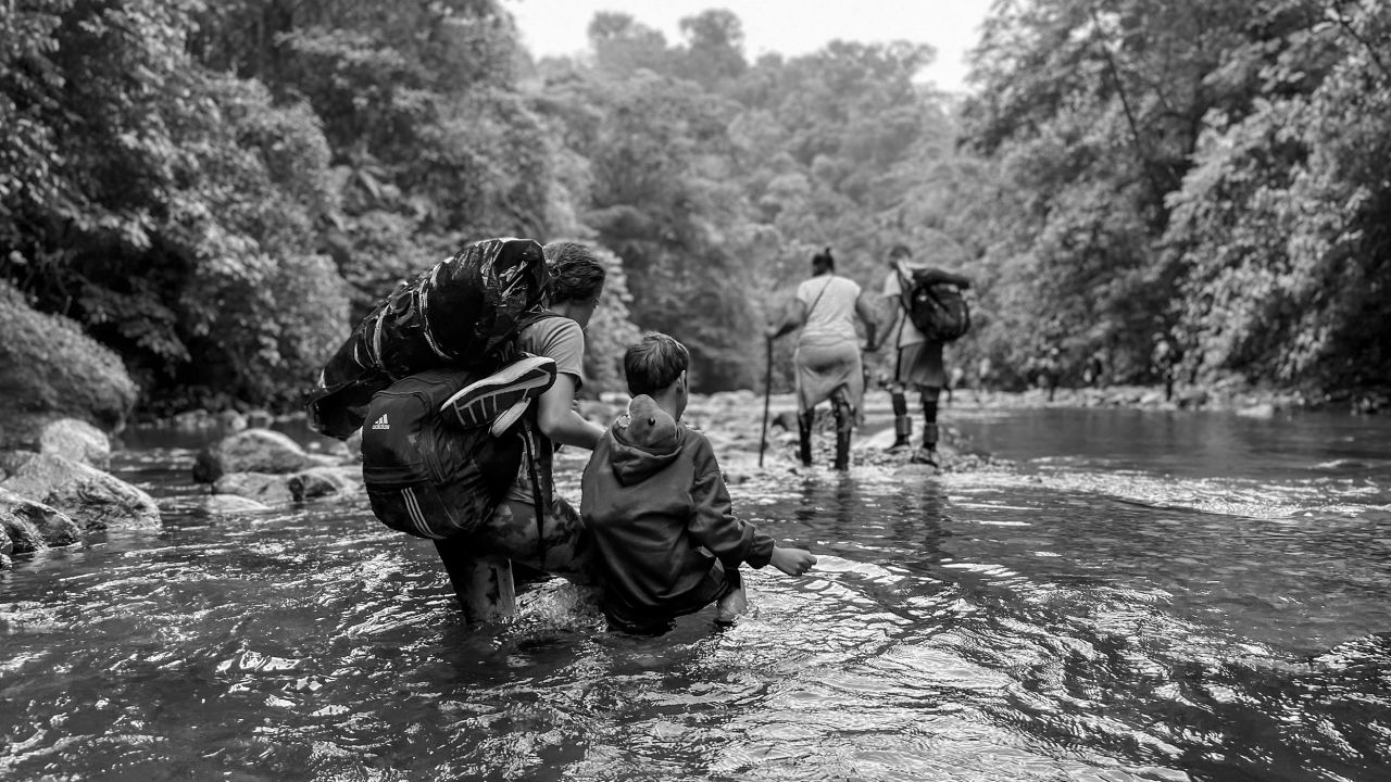 A Venezuelan woman guides her son through knee-high water, his dinosaur toy stuffed safely in his sweatshirt. She's hoping to get them to the US, to be reunited with her husband.